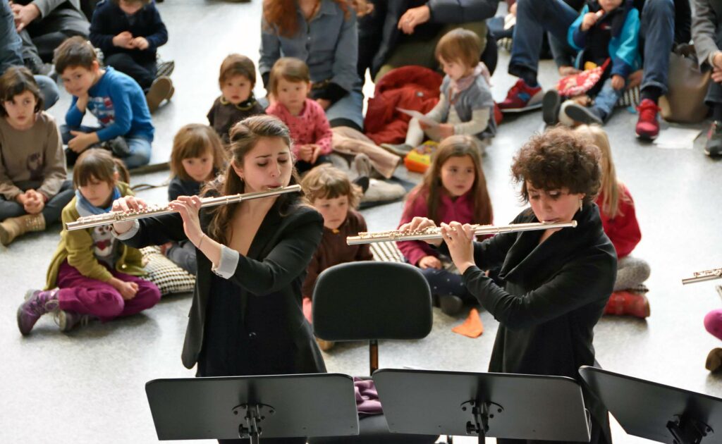 Hall in Musica: due flautisti suonano davanti a un pubblico di bambini seduti su cuscini.